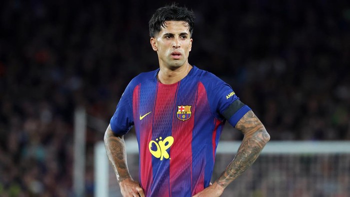 Soccer player in a Barcelona jersey with red and blue stripes standing on the field, hands on hips.