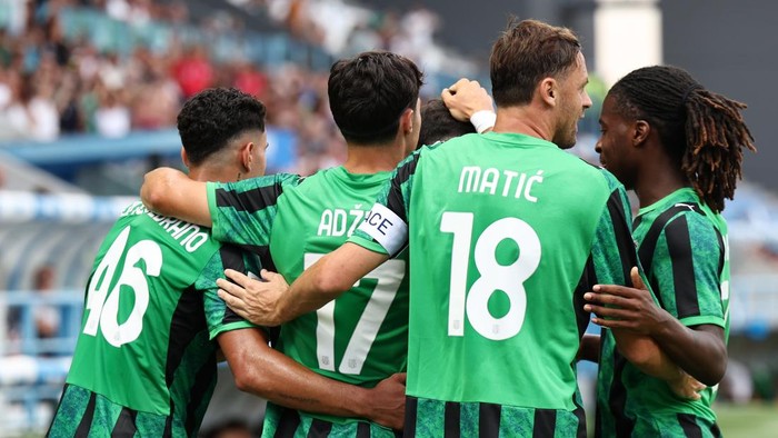 Soccer team in green jerseys huddling in celebration on the pitch.
