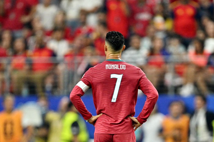 Soccer player seen from behind wearing a red jersey with the number 7 during a match in a crowded stadium.