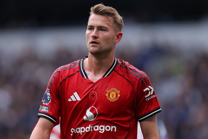 Footballer in a red Manchester United jersey on a pitch, looking off to the side.