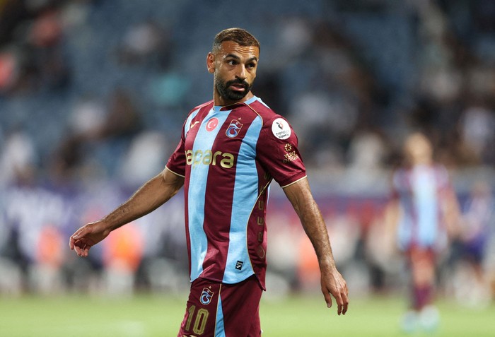 Footballer in maroon and light-blue striped jersey on a soccer field, looking to his left during a match.