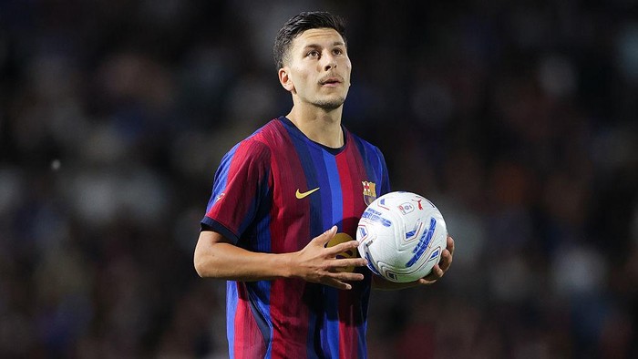 Soccer player in a maroon and blue striped jersey holding a white soccer ball on the field at night.