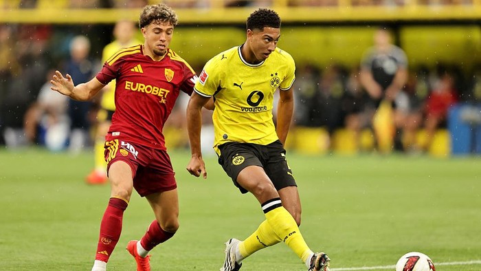 Two soccer players compete for the ball on a green field; one in red with Eurobet sponsor and the other in Borussia Dortmund yellow kit.