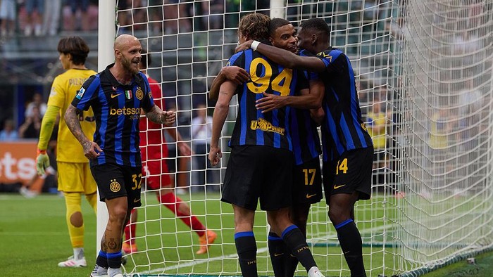 Football players in blue-and-black striped jerseys celebrate a goal near the net, hugging and smiling.