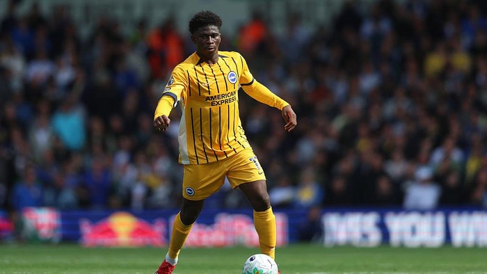 Soccer player in a yellow and black striped kit controls the ball on the pitch with a cheering crowd in the background.
