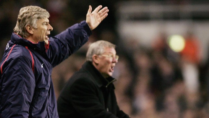 Two football coaches on the sideline shouting instructions, one with an arm raised.