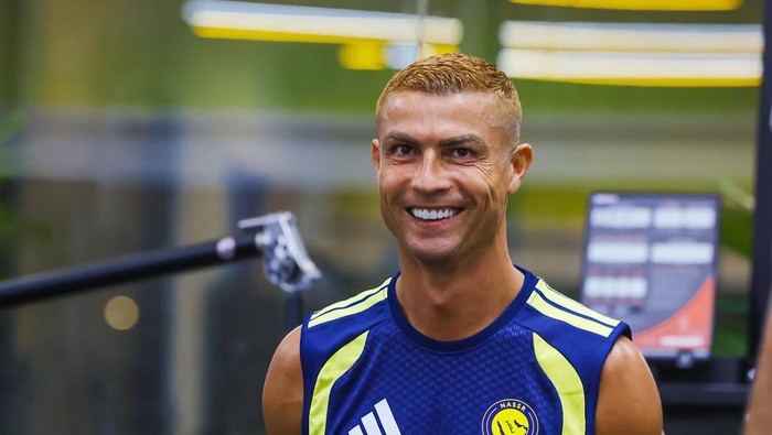 Smiling male athlete in a blue and neon-yellow training jersey inside a gym/studio setting.