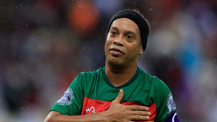 Soccer player in a green and red jersey with a black headband, hand over his heart on the field.