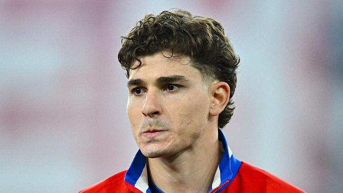Close-up of a male athlete in a red jacket with a blue collar, looking focused.
