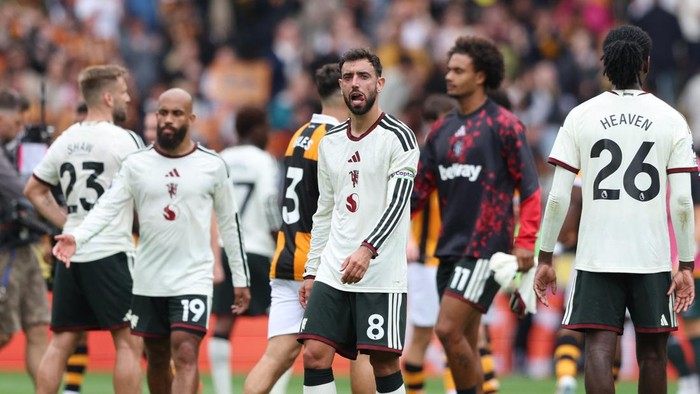 Group of soccer players in white kits on a pitch after a match; central player wearing number 8 glances toward the camera as teammates walk by.