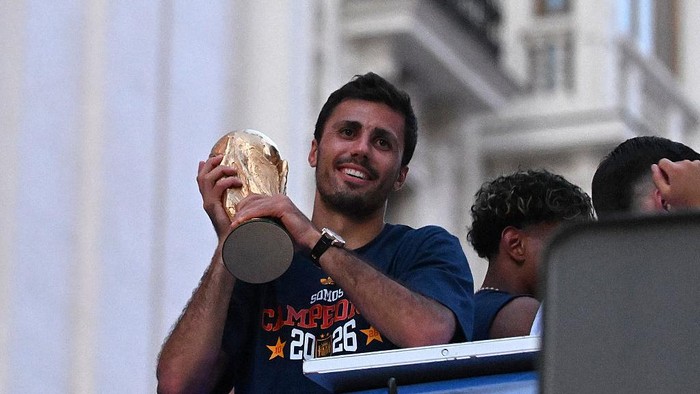 Man in a blue shirt lifts a trophy above his head and smiles on a podium moment of celebration.