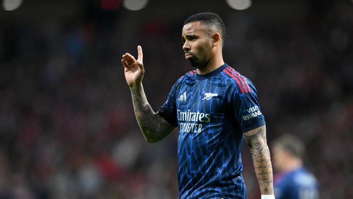 Soccer player in a blue Arsenal away kit raises his right hand on the field during a match, focus on him.