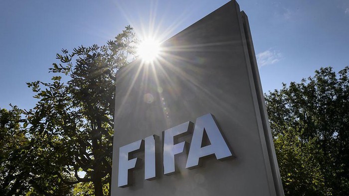 FIFA logo on a tall gray sign with sun glare behind and trees in the background