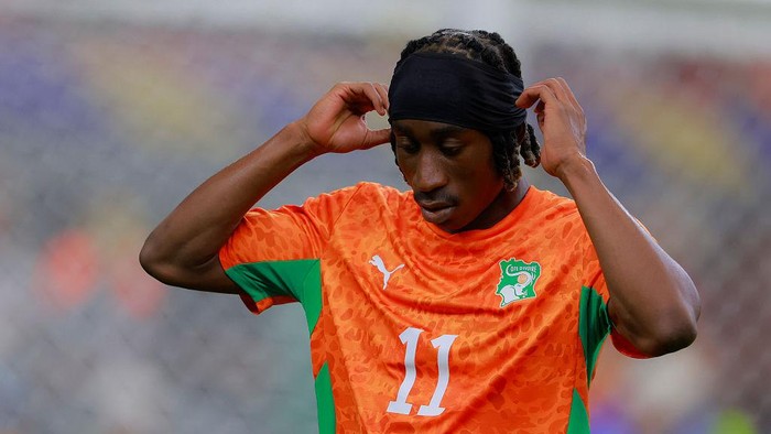 Soccer player in an orange jersey with number 11 adjusts a black headband during a game.