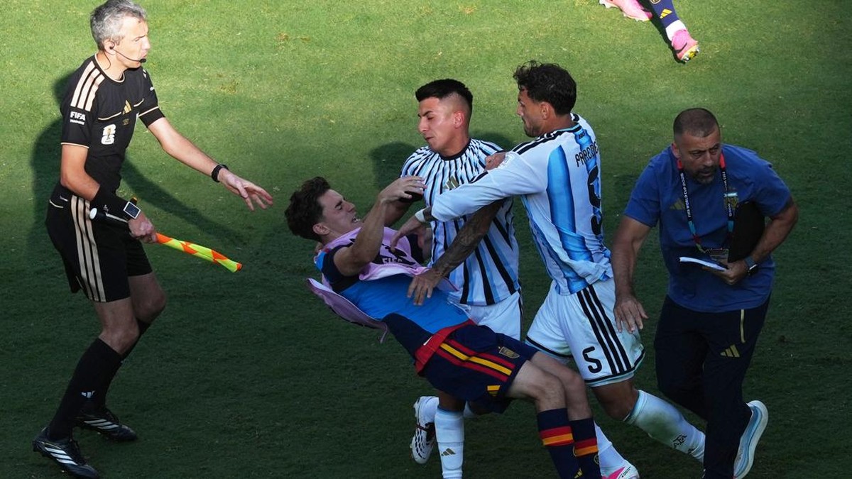 Assistant referee watches as players collide and fall during a soccer match on a green field.
