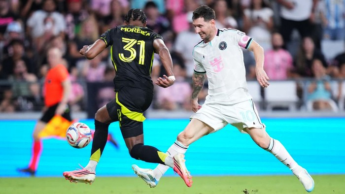 Two soccer players chase the ball during a match—one in a black kit (number 31) and one in white chasing from the right.