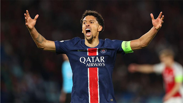 Soccer player in a PSG jersey raises arms in celebration, wearing a captain's armband.