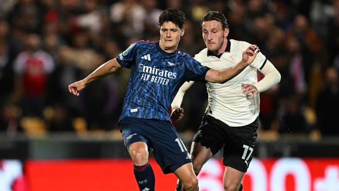 Two soccer players battle for the ball during a match; one in a blue Real Madrid kit and the other in a white jersey, crowd in background