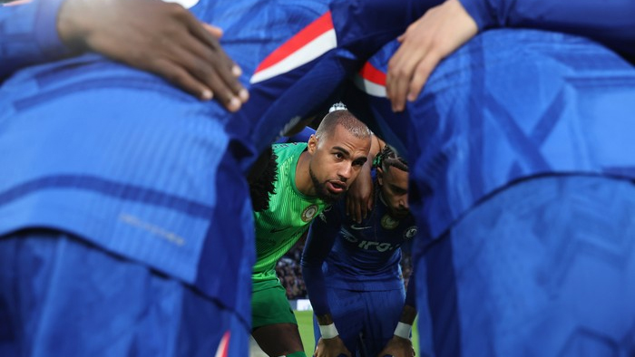 Soccer players form a human tunnel in blue, with a green-clad goalkeeper peering through with a focused look coming from the tunnel entrance before a match.