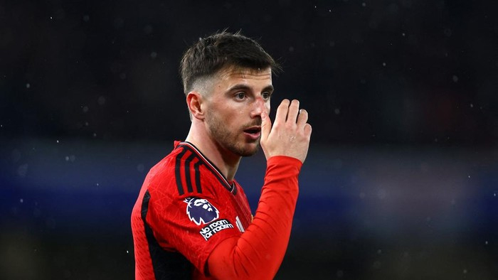 Soccer player in a red jersey touching his face during a match, night game with rain.
