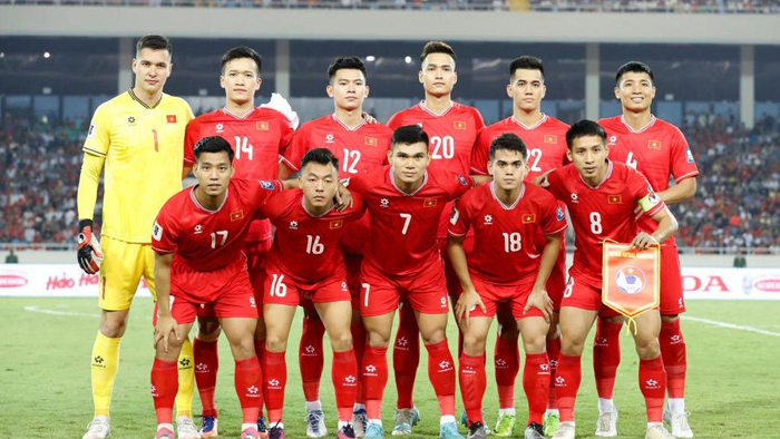 Vietnam national football team in red jerseys posing for a group photo on the pitch, goalkeeper in yellow at the left.