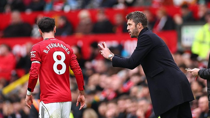Football manager shouting instructions at a player in a red jersey on the field.