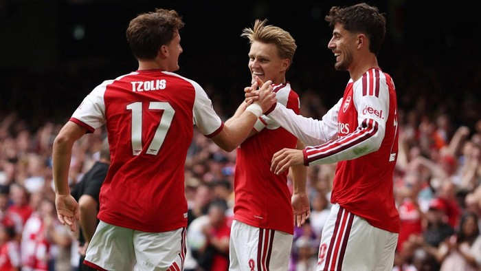 Arsenal teammates celebrate a goal with a high-five on the pitch; Tzolis #17 visible on one jersey.
