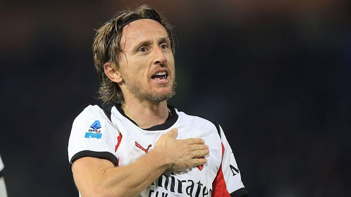 Soccer player in a white jersey places his right hand over his chest during a match.”,