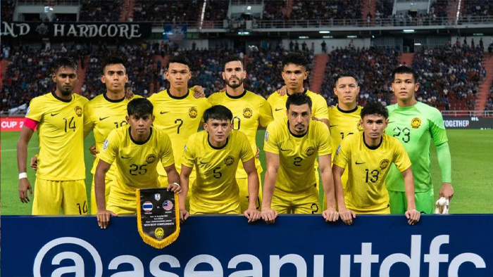 Eleven-member national soccer team in yellow jerseys pose for a group photo on the field behind a blue banner, with the goalkeeper in a green kit on the right.