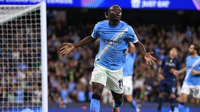 Soccer player in a blue kit celebrates a goal with arms outstretched near the goal.