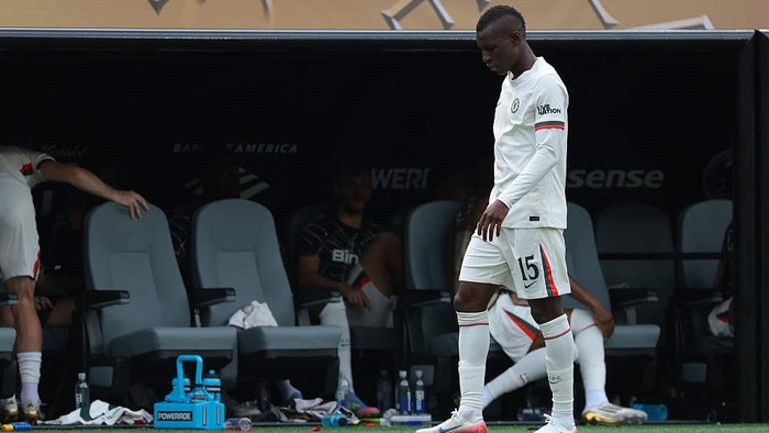 Soccer player in white kit with number 15 walking past the team dugout on the sideline during a match.