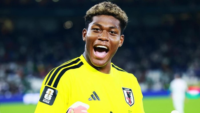 Male soccer goalkeeper in a bright yellow Japan national team jersey celebrating on the field.