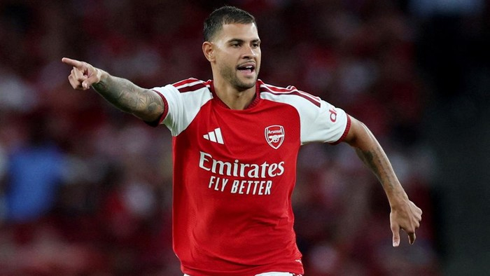 Arsenal forward pointing and shouting on the pitch in a red home kit with Emirates Fly Better sponsor.