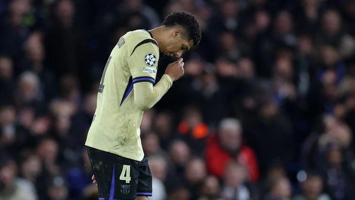 Dejected footballer in a light beige jersey with the number 4, head bowed on the pitch with fans in the background.