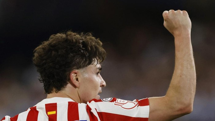 Soccer player in a red-and-white striped jersey raises a clenched fist in celebration.