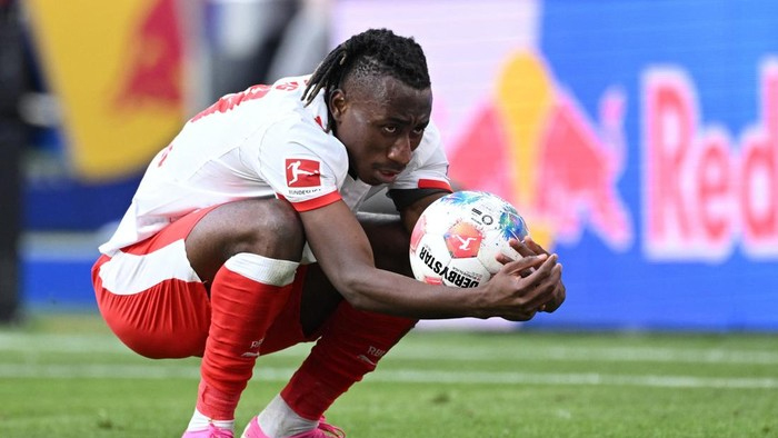 Soccer player in a white and red kit crouches on the field, holding a ball against his chest near the sideline advertising boards.