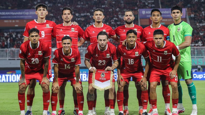 Indonesian national football team posing for a group photo in red uniforms on the field, goalie in green on the right.