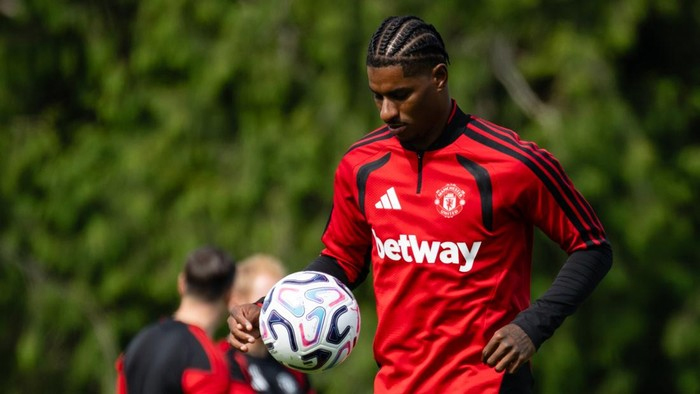 Soccer player in a red Manchester United training kit controls a ball during practice on a green field.