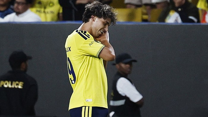 Soccer player in a bright yellow jersey with number 9 stands on the field, hands raised to his face in a moment of emotion.