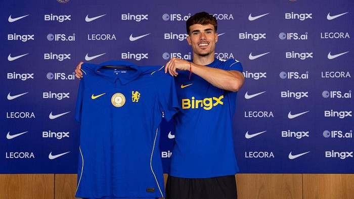 Soccer player in a blue kit holds up a blue polo shirt with the club crest, standing in front of a backdrop full of BingX logos.