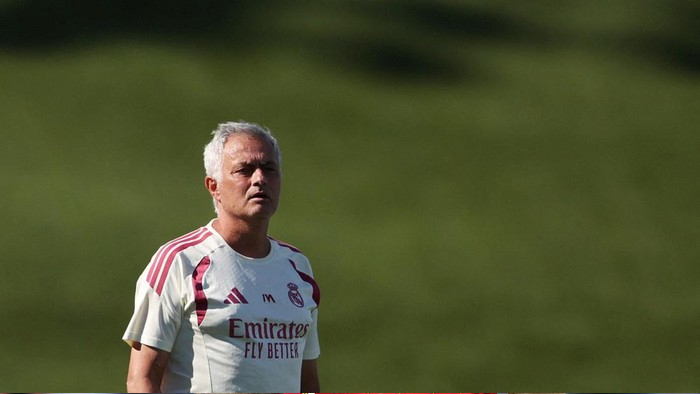 Older man in a Real Madrid white jersey standing on a grassy field, looking ahead.