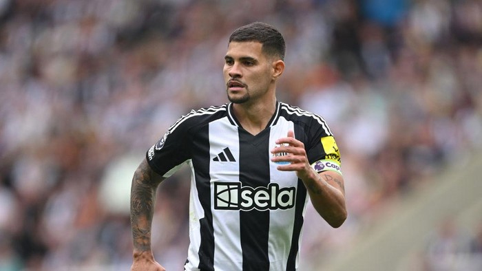 Soccer player in a black-and-white striped kit running on the field, with a yellow captain's armband.