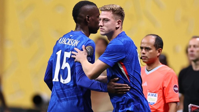 Two soccer players in blue jerseys hug on the field, one with number 15 and name Jackson on his back, as they celebrate or console each other.