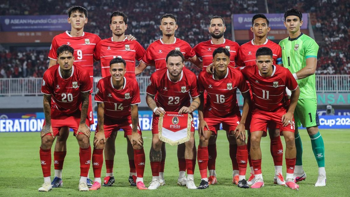 Indonesian national football team posing for a group photo on the pitch in red uniforms, with the goalkeeper in green on the far right.