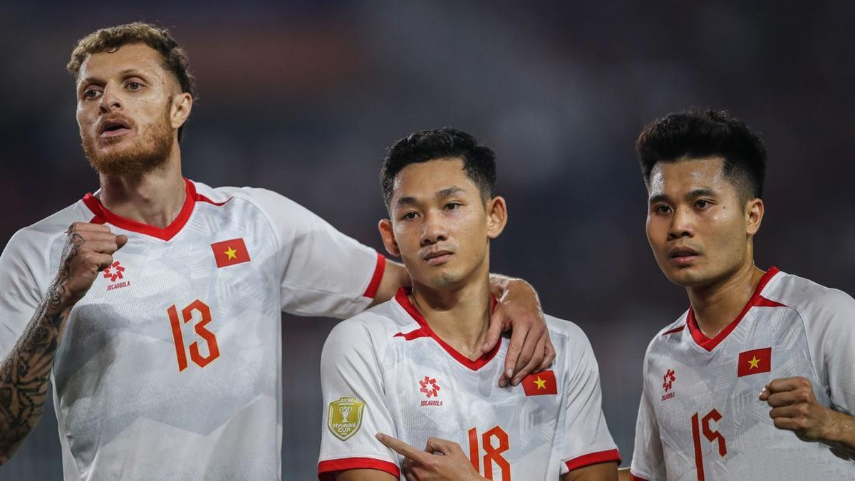 Three Vietnamese footballers in white jerseys with red trim pose together on the field, arms around each other after a match.