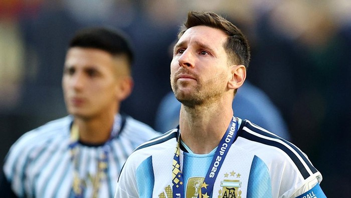 Lionel Messi in Argentina jersey with a winner's medal and lanyard, looking upward on the pitch.