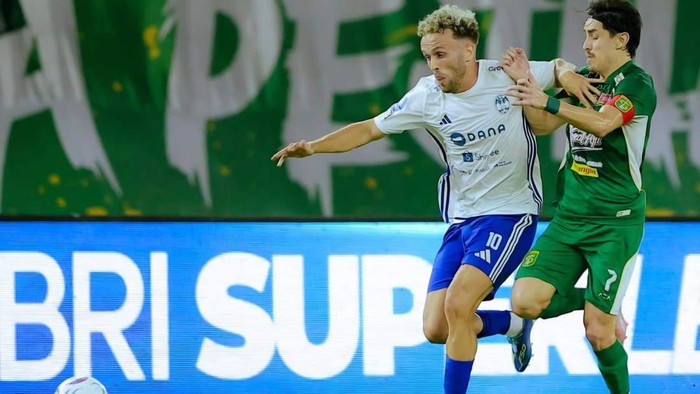 Two soccer players chase the ball during a match, one in white and blue and the other in green, battling for possession.