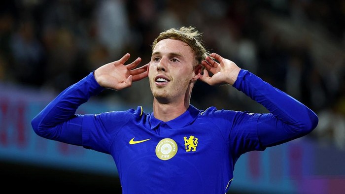 Soccer player wearing a blue Chelsea jersey cupping his ears in celebration after scoring a goal.