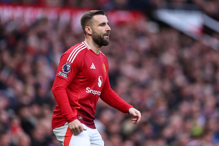 Manchester United footballer in a red kit walking on the pitch during a match, with a blurred crowd in the background.