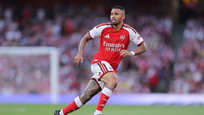 Arsenal footballer in red kit sprinting on the pitch during a match, stadium blurred in the background
